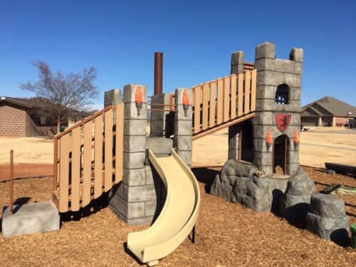 Castle themed playground structure on top of rocks w/climbers, nets, and slides