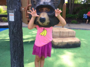A little girl at a playground structure behind an animal face of a bear
