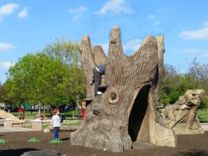 Tunnel Stump Tree Climber in a playground with kids climbing atop it on a bright sunny day.